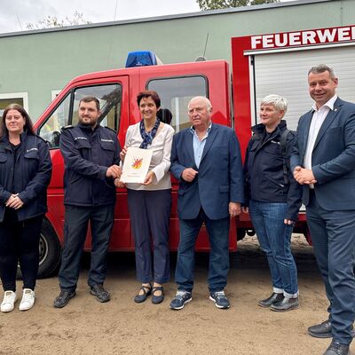 Foto 1: Landrat Michael Sack bei der &Uuml;bergabe des Zuwendungsbescheides an Penkuns B&uuml;rgermeisterin Antje Zibell (3.v.l.) und Mitglieder der Freiwilligen Feuerwehr Penkun im Beisein des Penkuner Ehrenb&uuml;rgers Hans-Ullrich Wegner